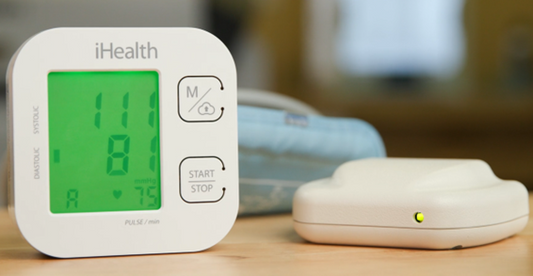 A blood pressure cuff sits on a table beside a VITAdLS Gateway - a palm-sized white device. 