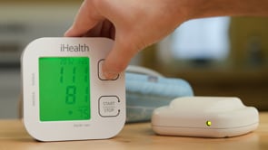 A man unboxes an arm blood pressure cuff and then takes his blood pressure. 